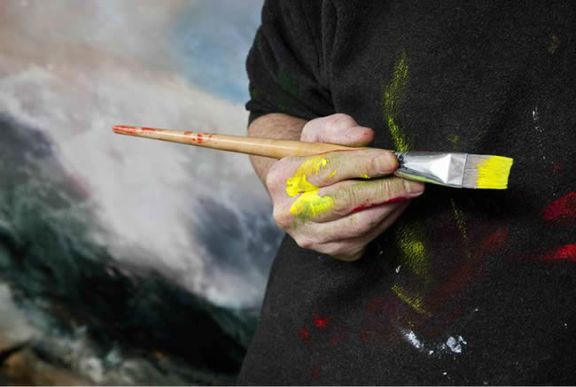 Artist in studio poised with brush in hand