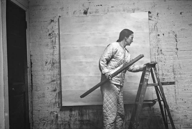 Agnes Martin stands in an art studio with level and ladder