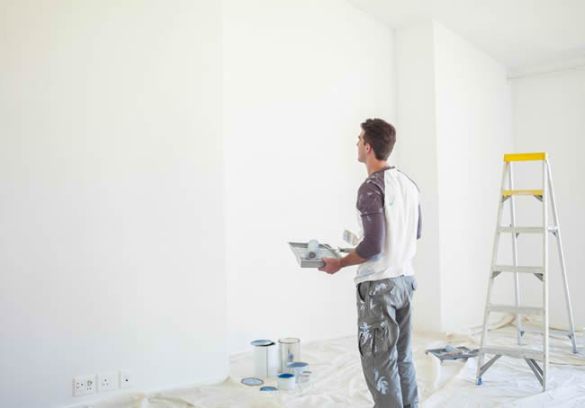 Man with paint tray looking up at white wall