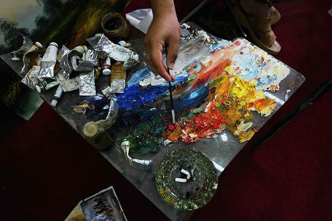 An Iraqi painter dabs his brush on a palette
