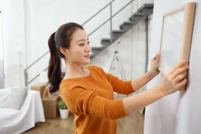 woman hangs picture frame on wall