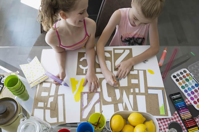 Girls making lemonade sign with stencils at dining table