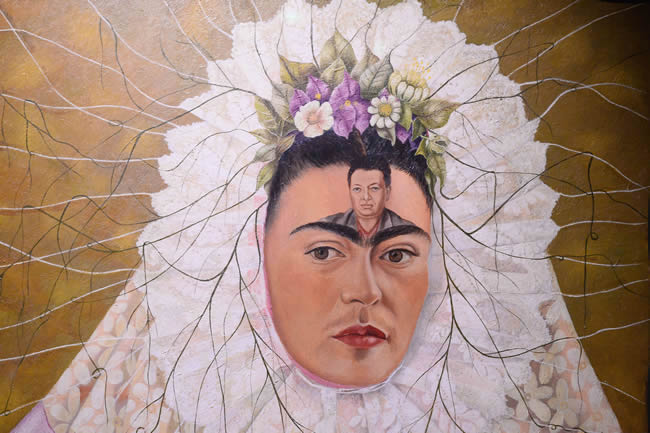 Portrait of Frida Kahlo in a white headdress with a portrait of Diego Rivera engraved on her forehead.