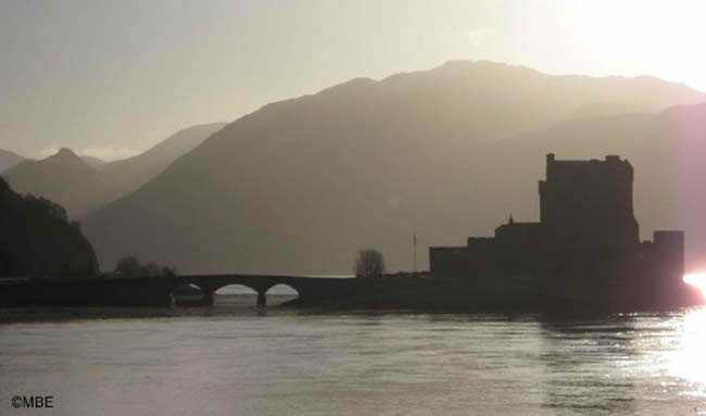 Eileen Donan Castle Dornie in the Scotland Highlands silhouetted against a bright sky.