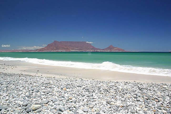 Rocky beach and turquoise water with Table Mountain in the background.