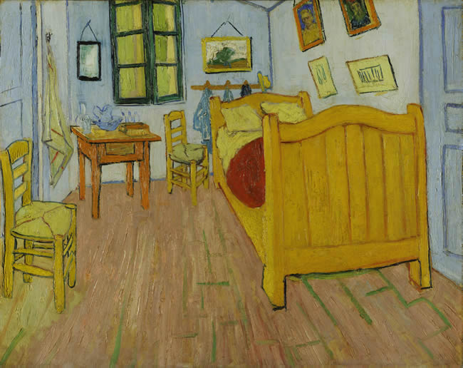 Small bedroom with blue walls, yellow bed, two wicker chairs and a small table.