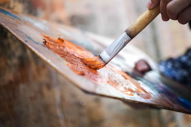 painter applying paint to a brush on a palette