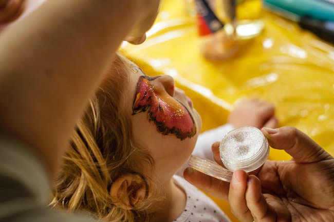 Painting a young child's face, emphasis on glitter paint.