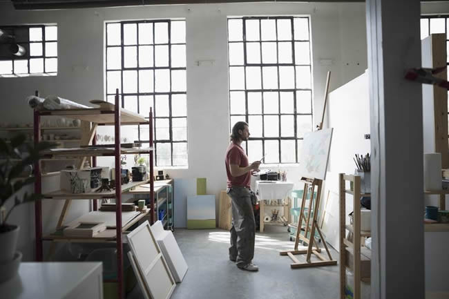 Male painter painting at canvas on easel in art studio