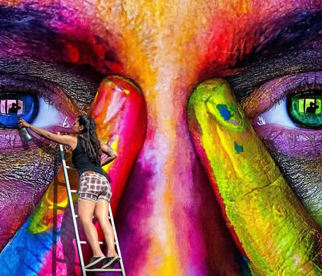 Female artist on a ladder painting with spray paint.